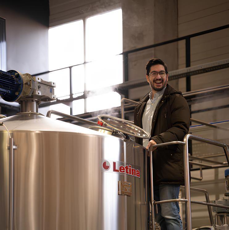 Smiling happy person next to a metal keg in a beer factory