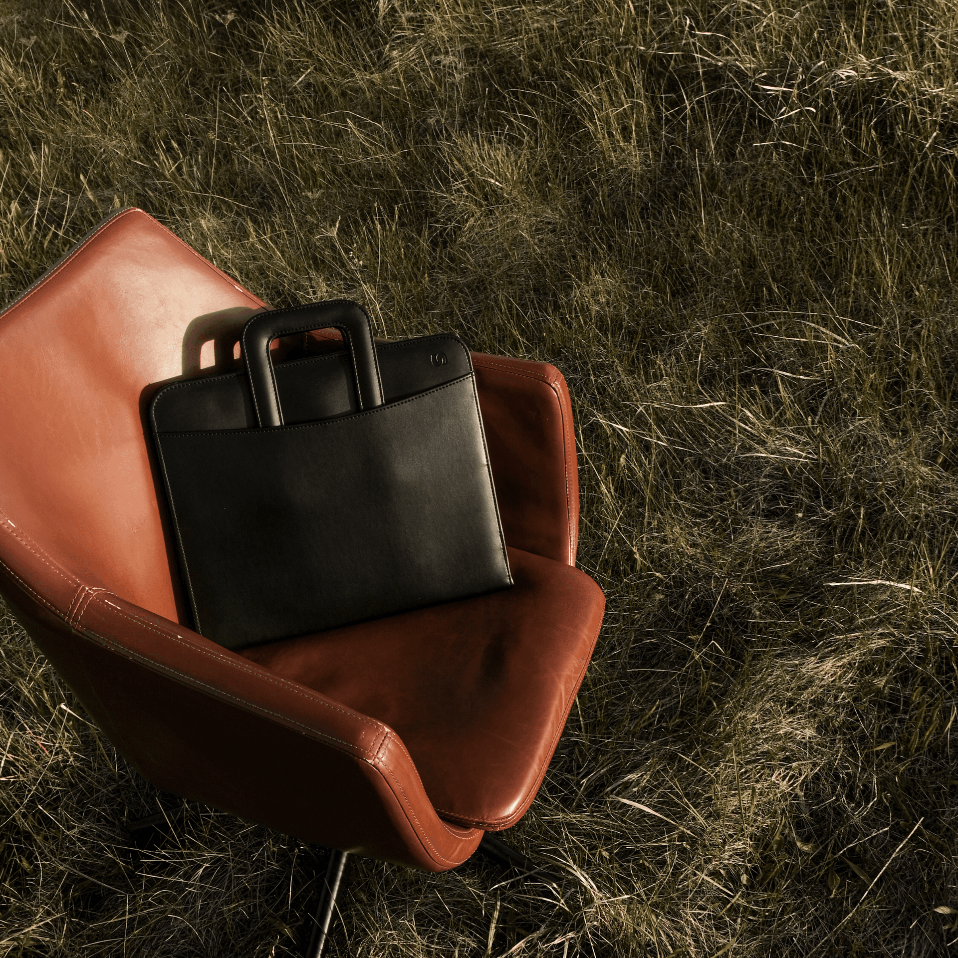 Black leather briefcase on a brown leather office chair on a grass field