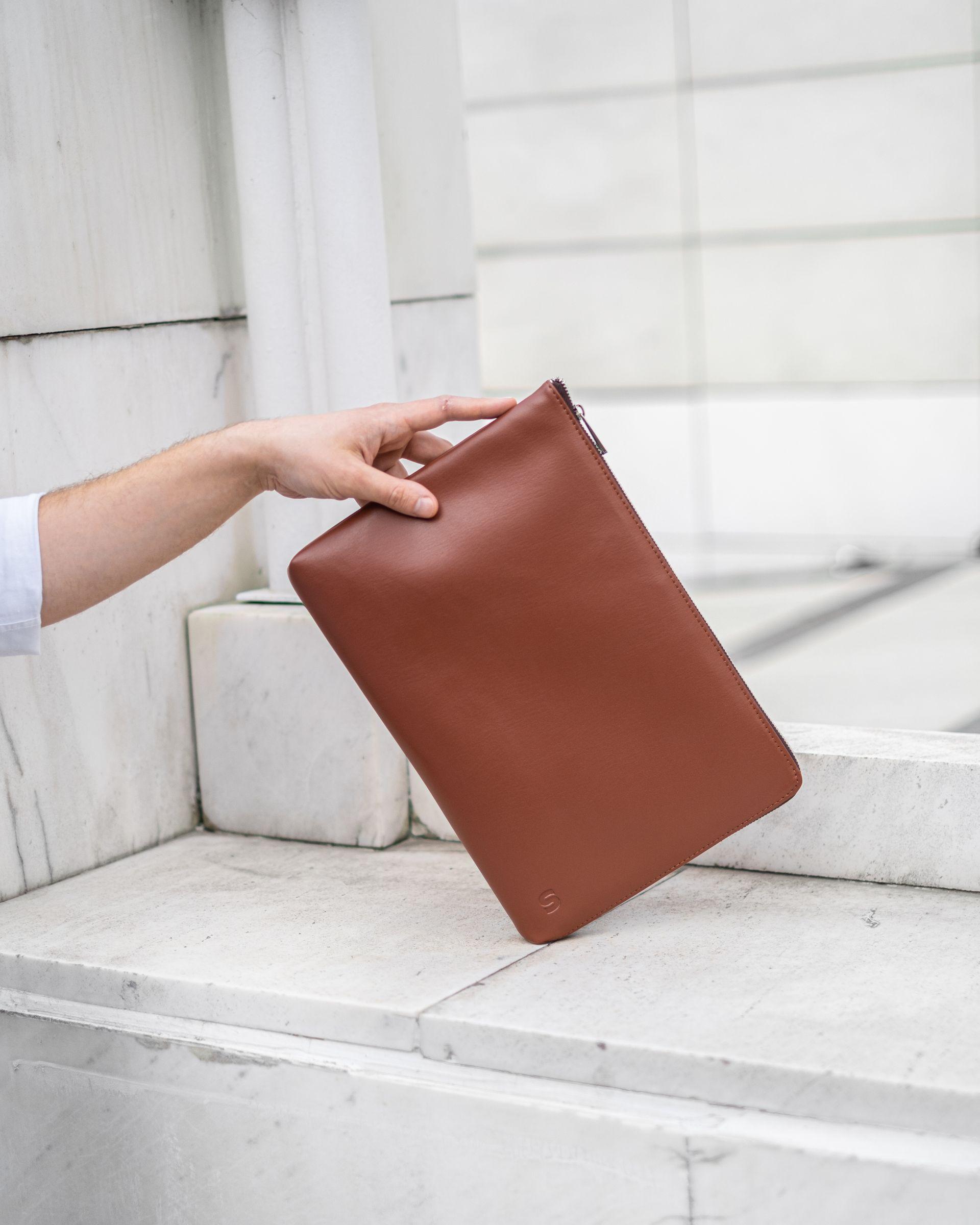 Hand holding a brown leather laptop case