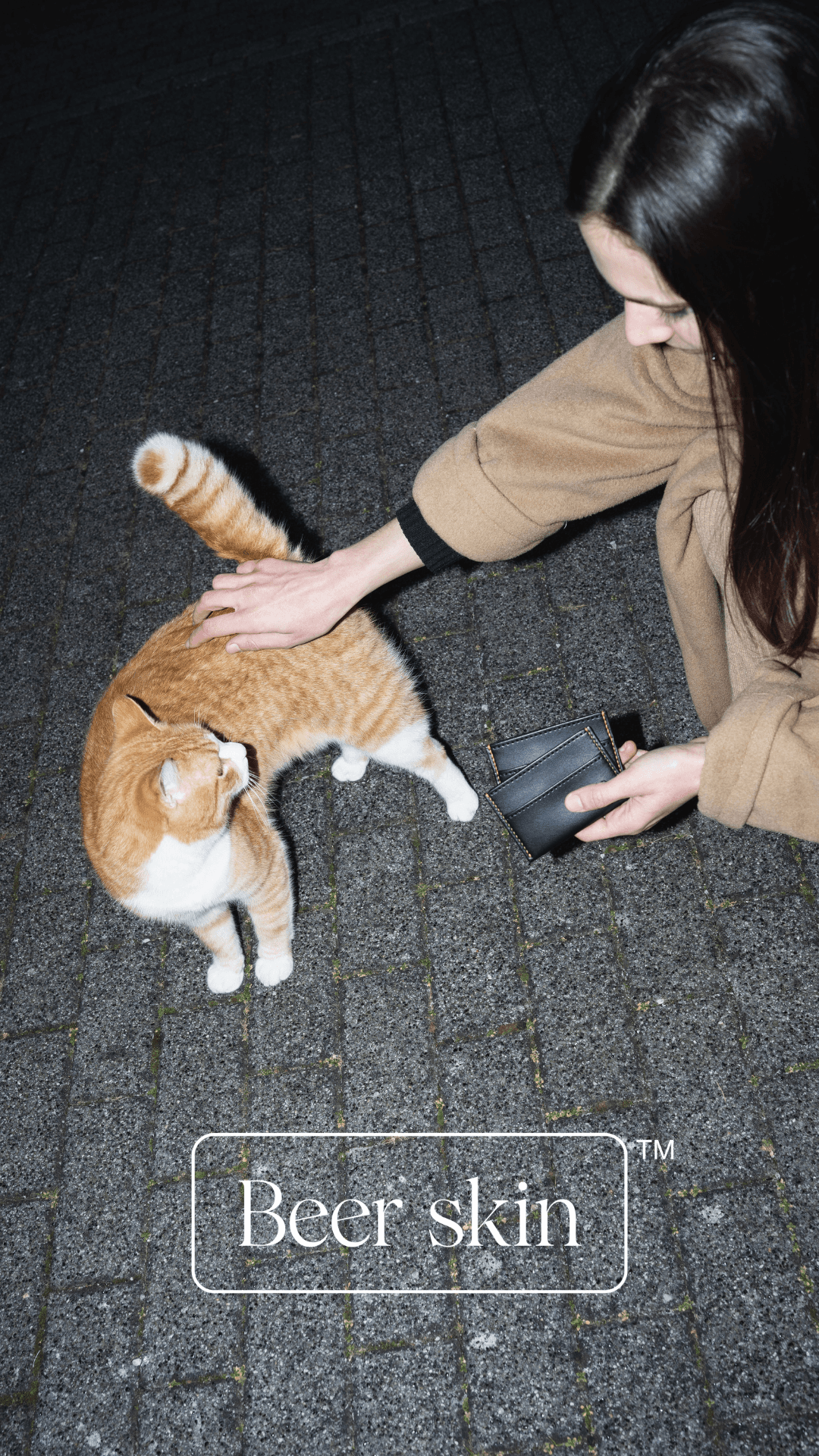 Female model holding a black leather wallet petting an orange cat