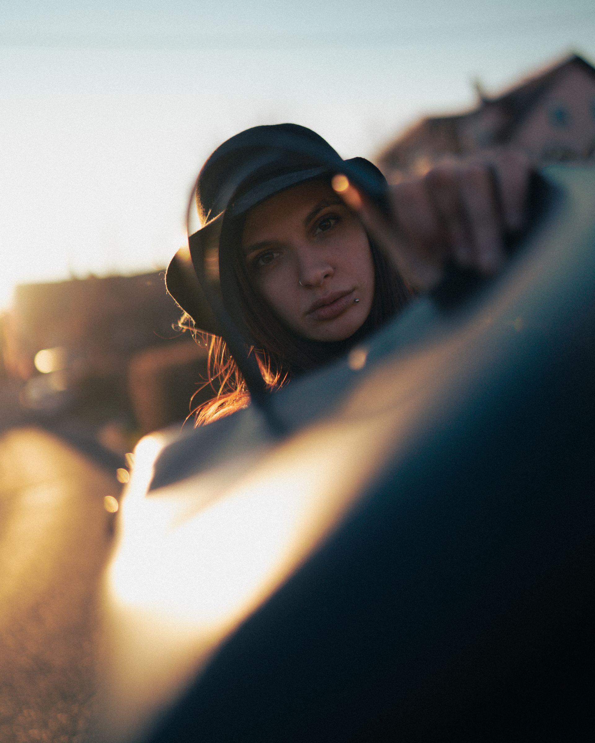 Female model with piercings and hat holding a leather bag on sunset