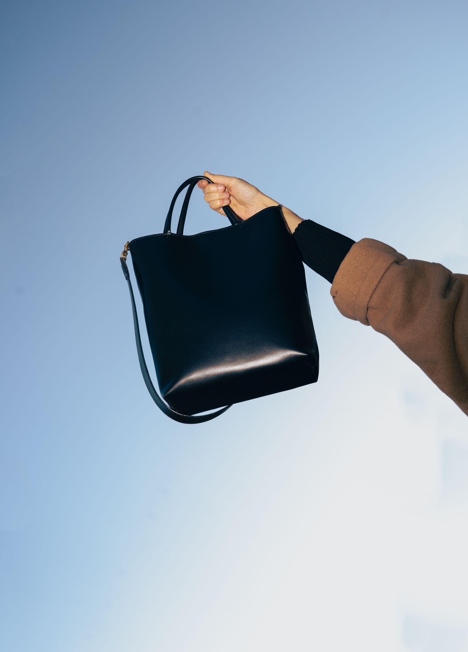 Black leather plant based handbag being held in hand with blue sky